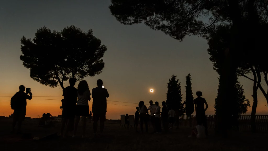 Fotografía del eclipse solar desde la explanada del Castillo de la Mota, en Medina del Campo, con las siluetas de varias personas observando el fenómeno al atardecer.