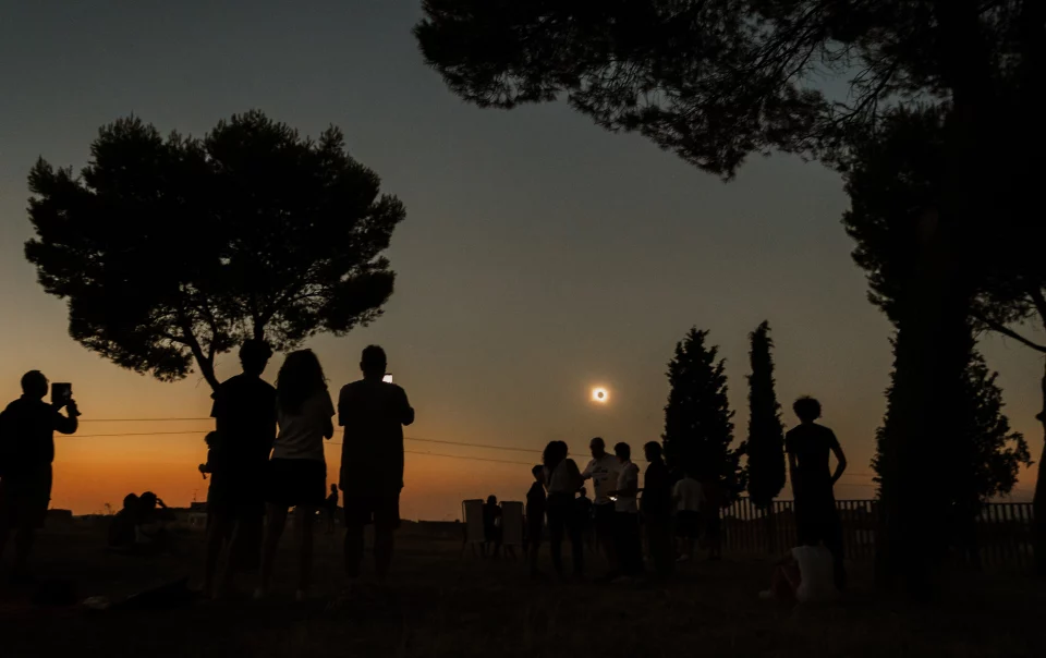 Fotografía del eclipse solar desde la explanada del Castillo de la Mota, en Medina del Campo, con las siluetas de varias personas observando el fenómeno al atardecer.
